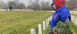 Woman holding wreathes salutes in front of a gravestone.